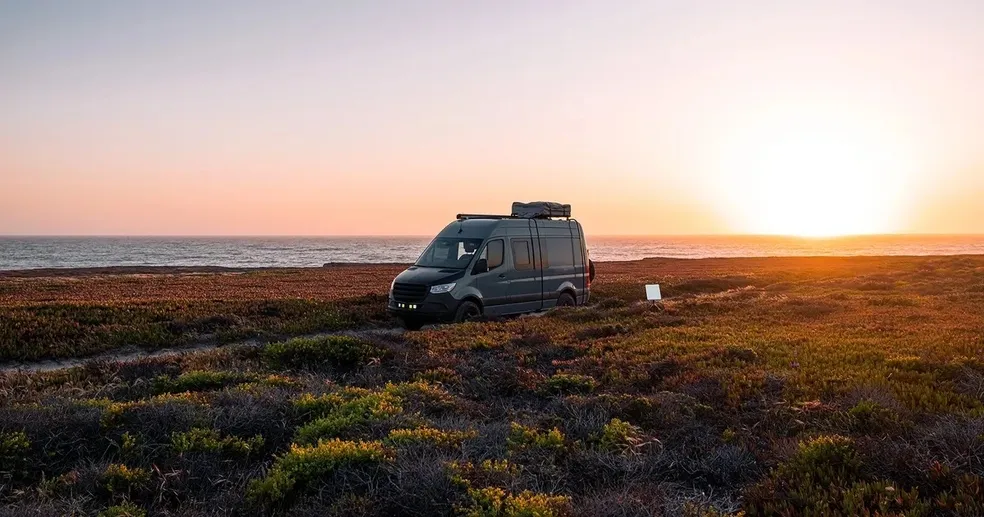 A van parked on the beach at sunset.