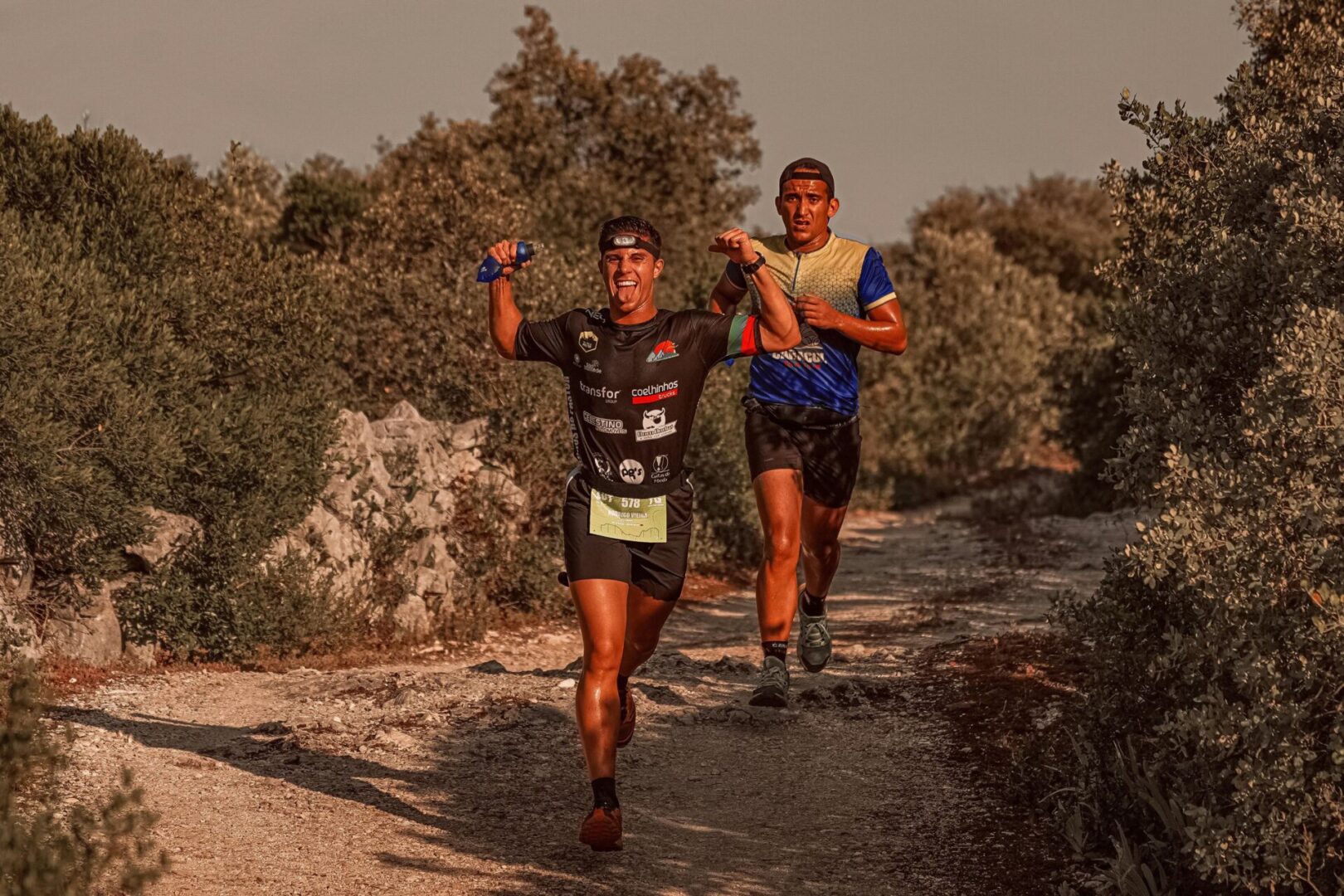 Two men running on a dirt path near trees.